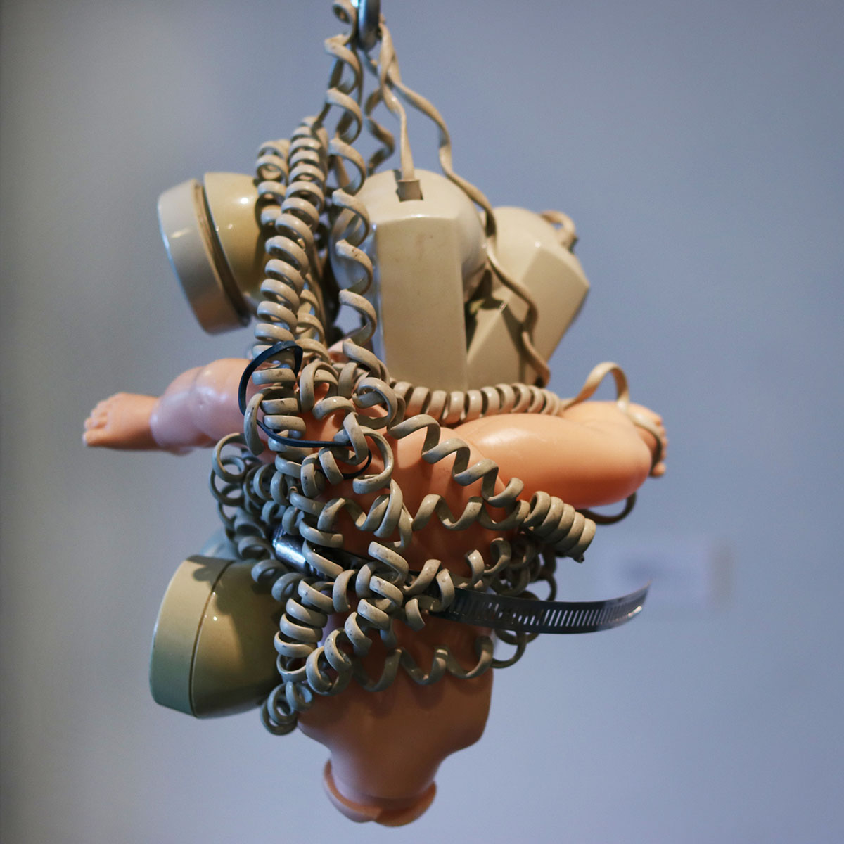 A hanging sculpture of doll arms tangled in phone wires and phones heads.