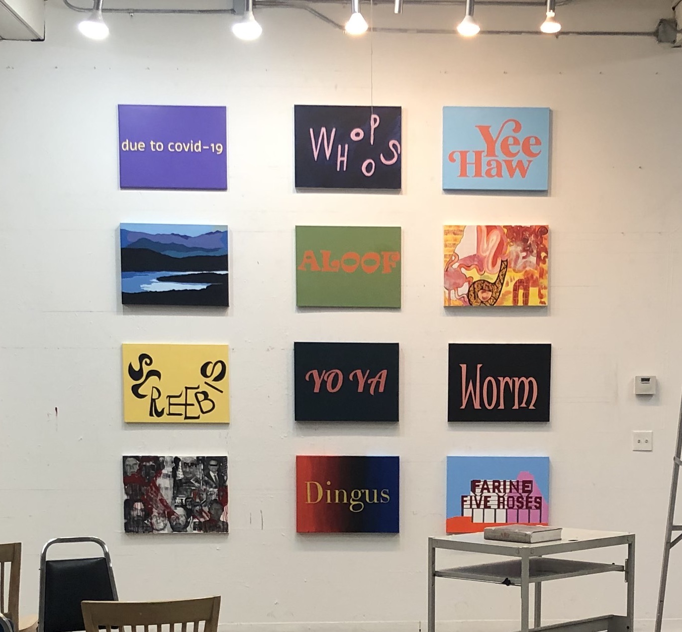 12 acrylic graphic paintings hang on the wall. They all say different words or phrases.